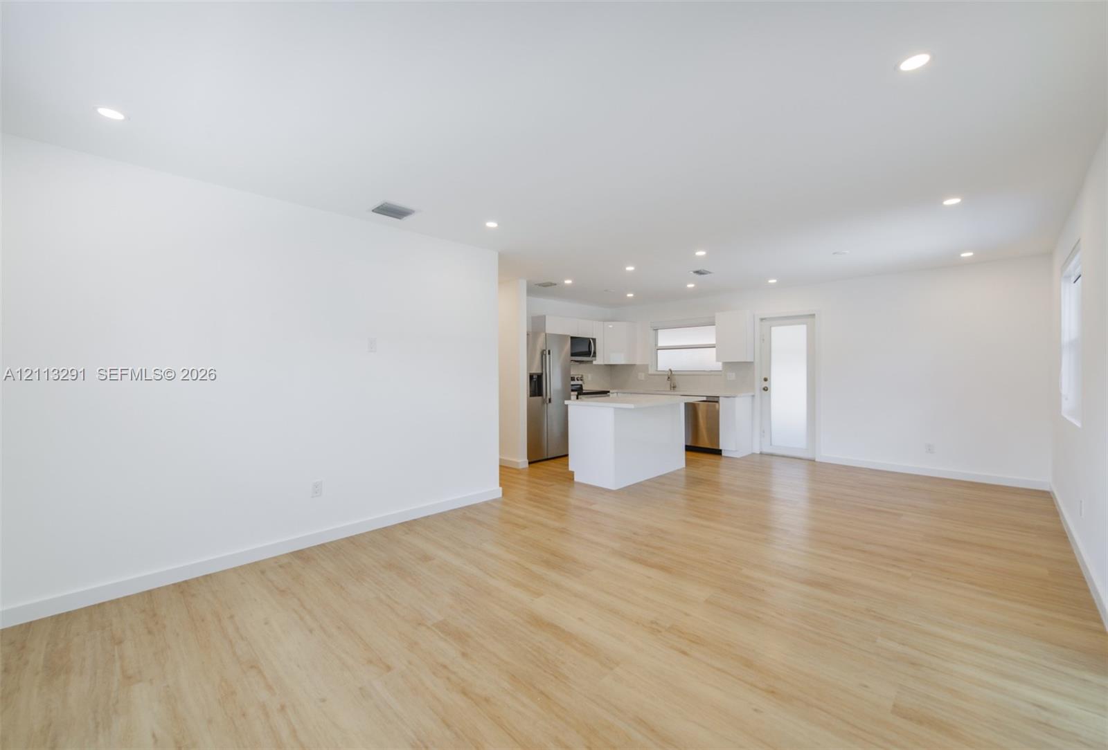 Open floor plan featuring wood-finish flooring, recessed lighting, white cabinetry, a center island, and stainless steel appliances