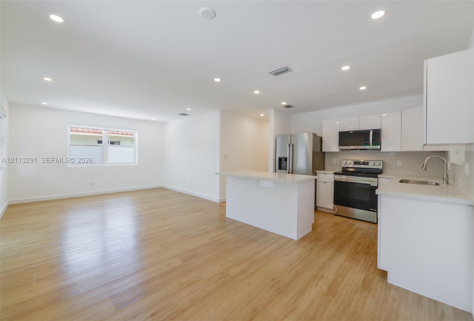 Kitchen featuring white cabinetry, solid-surface countertops, stainless steel appliances, wood-finish flooring, and recessed lighting