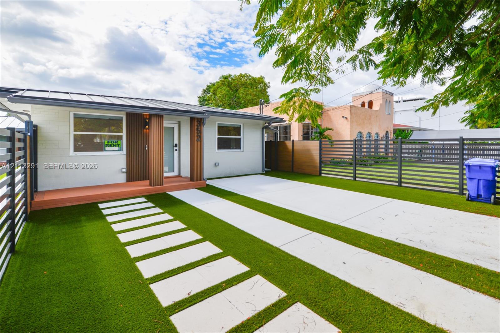 Exterior facade featuring a metal roof, synthetic turf lawn, concrete paver pathway, and horizontal privacy fencing Exterior facade featuring a metal roof, synthetic turf lawn, concrete paver pathway, and horizontal privacy fencing
