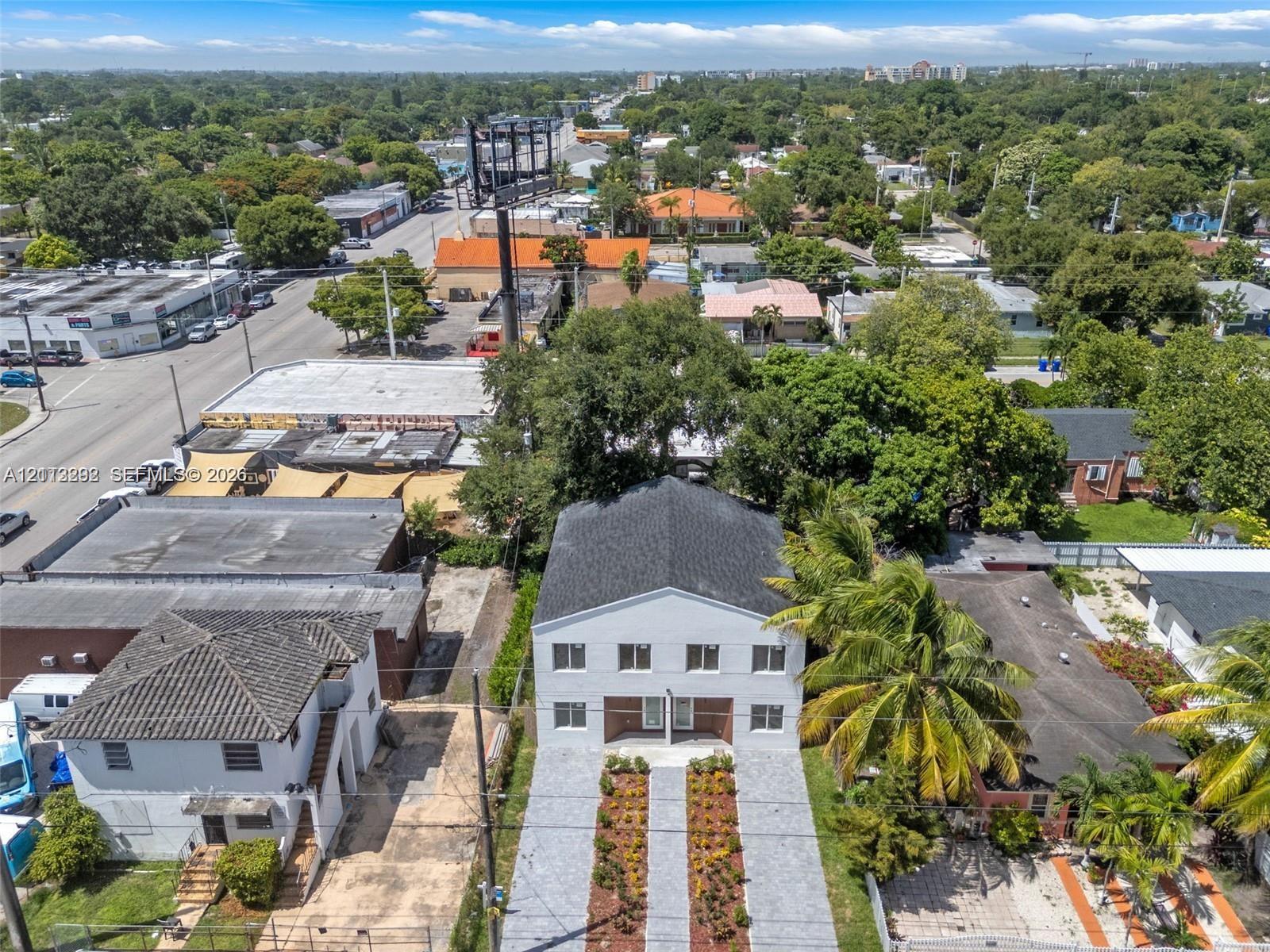 Two-story multi-unit building featuring a white facade, gabled roof, paved dual-track driveway, and curated landscaping