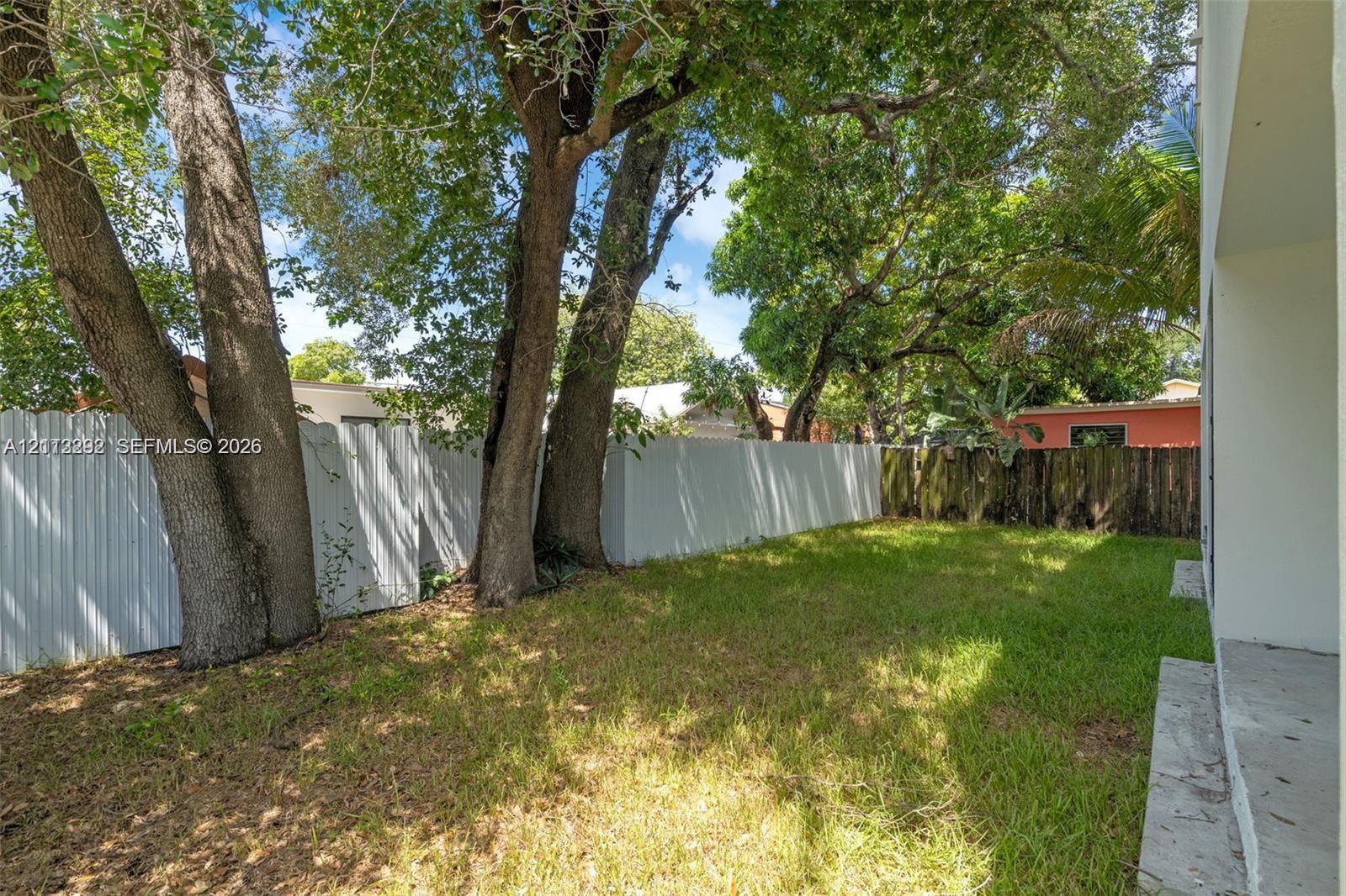 Rear yard featuring mature trees, a concrete patio, and a white privacy fence