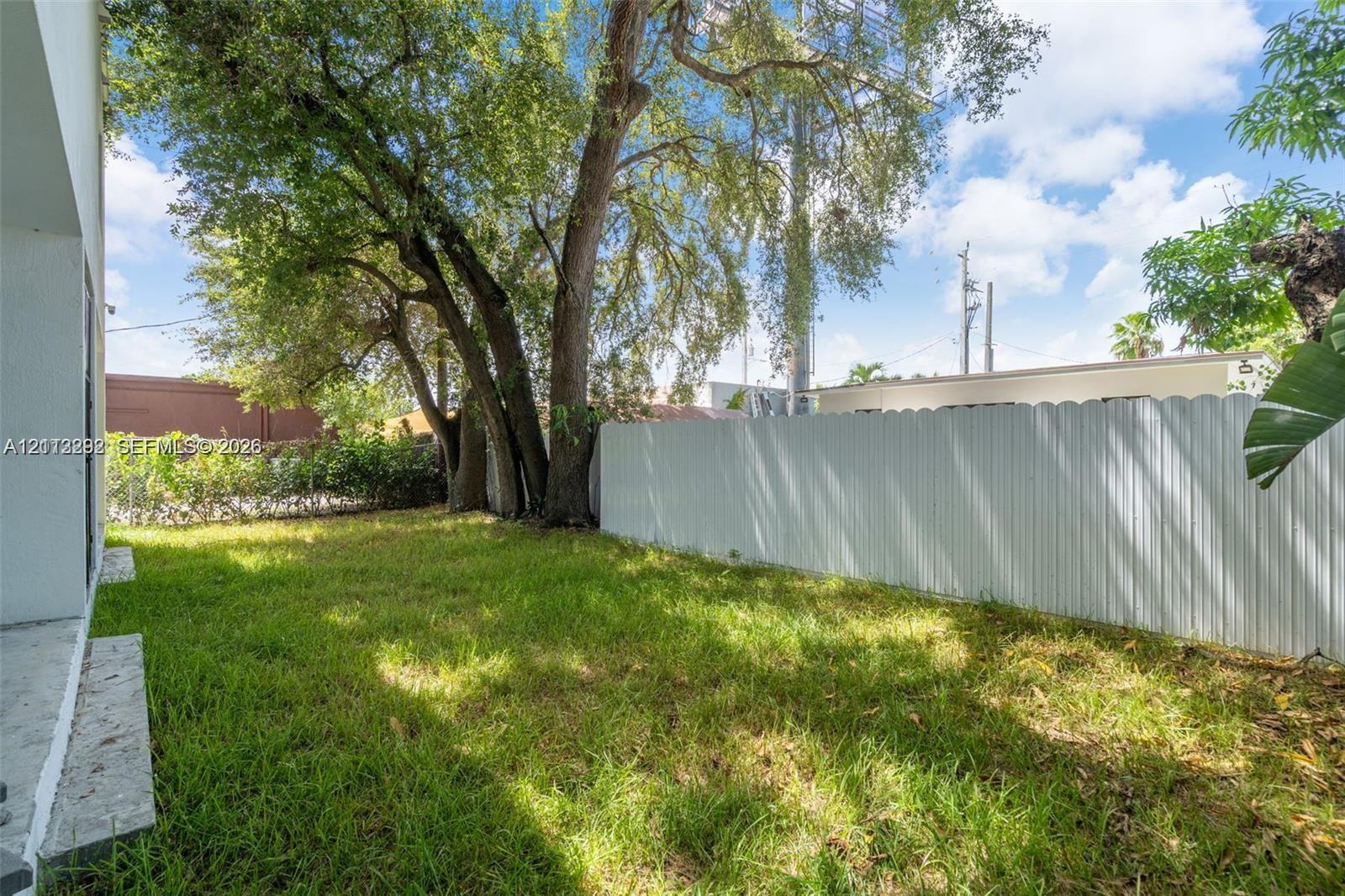 Private backyard featuring mature trees, grass lawn, and white corrugated metal fencing