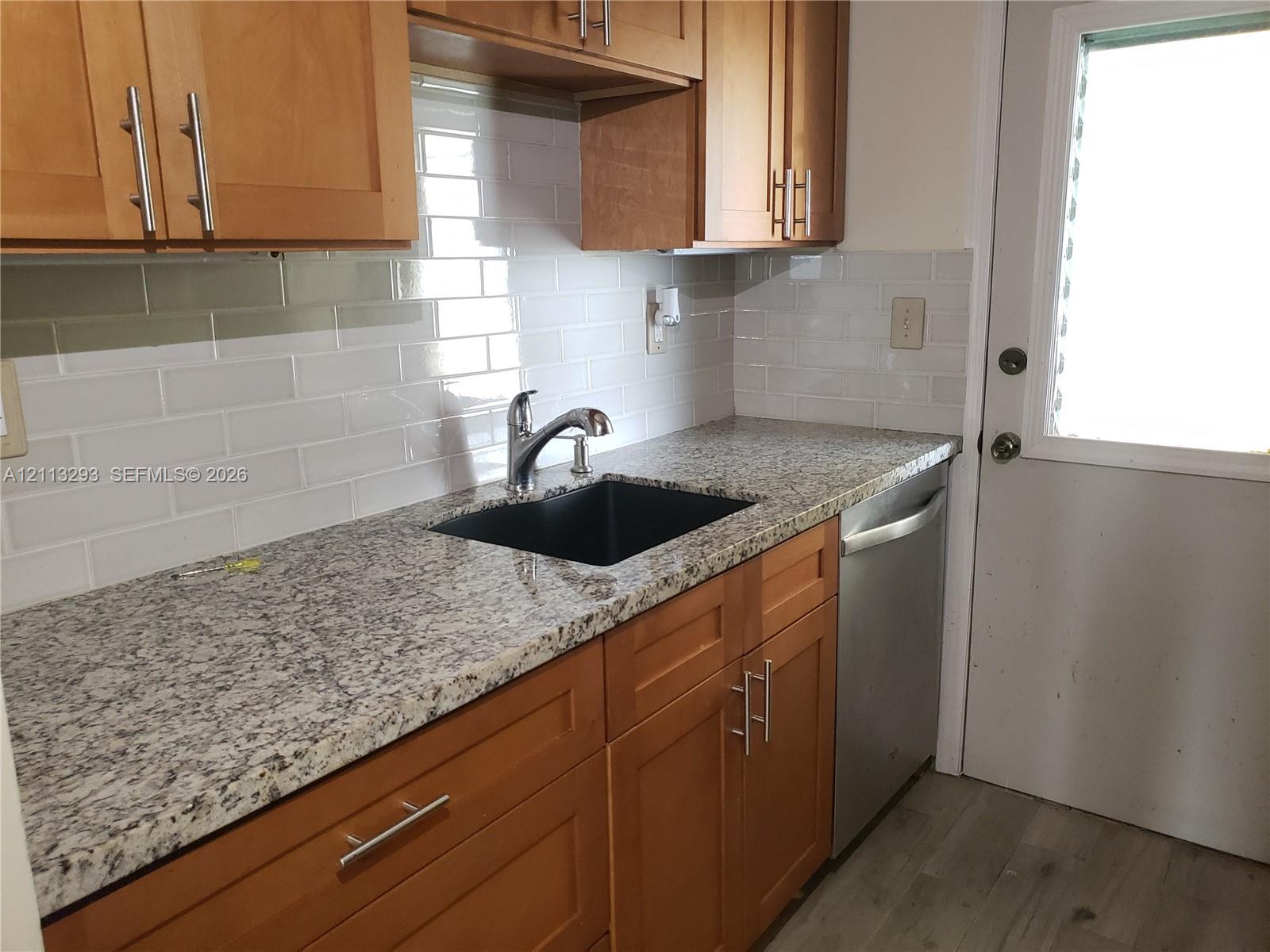 Kitchen featuring wood cabinetry with brushed nickel hardware, stone-finish countertops, white subway tile backsplash, a black undermount sink with a gooseneck faucet, and a stainless steel dishwasher
