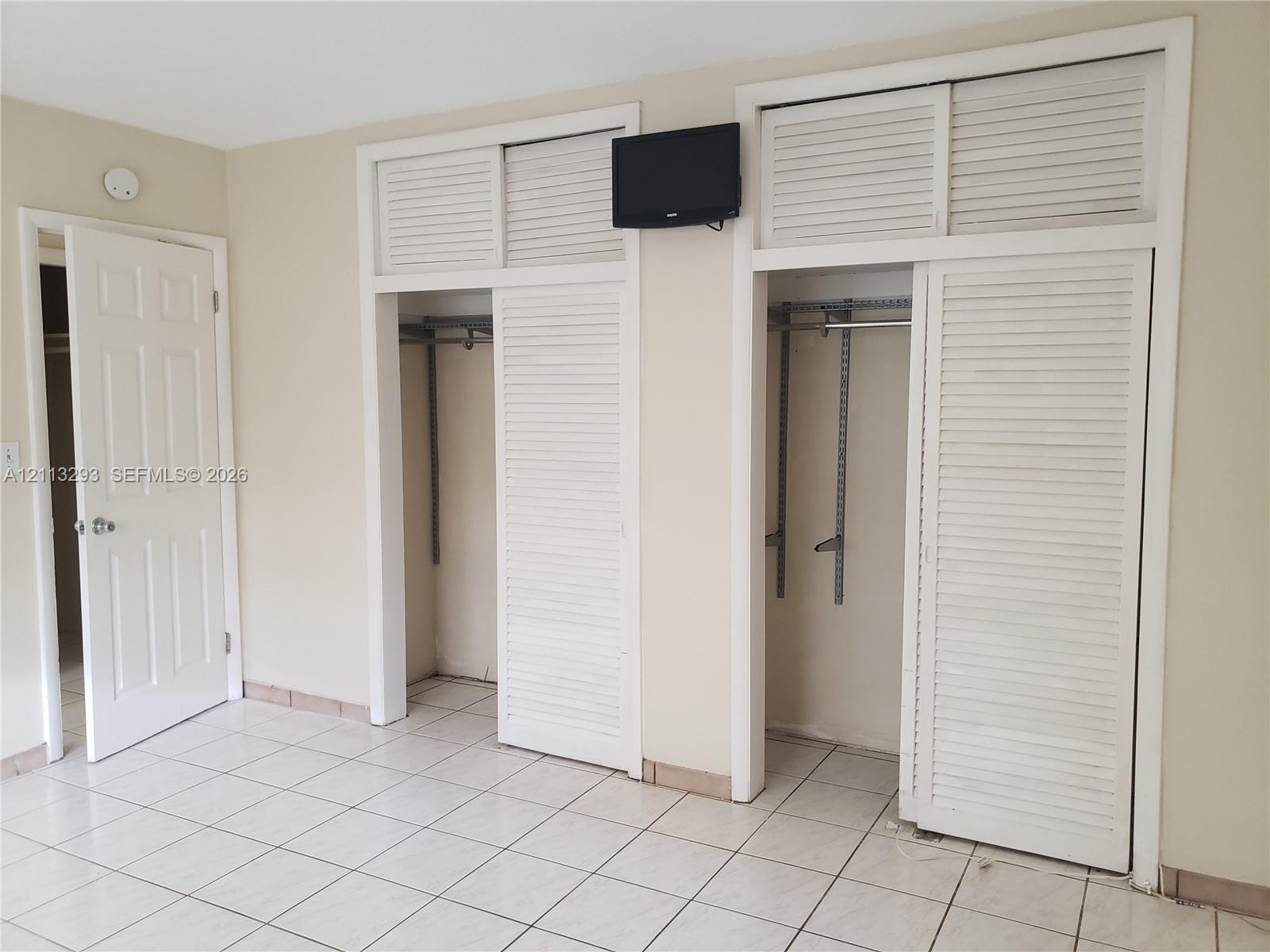 Ceramic tile flooring throughout and two dual-closet units featuring white louvered sliding doors and overhead storage compartments