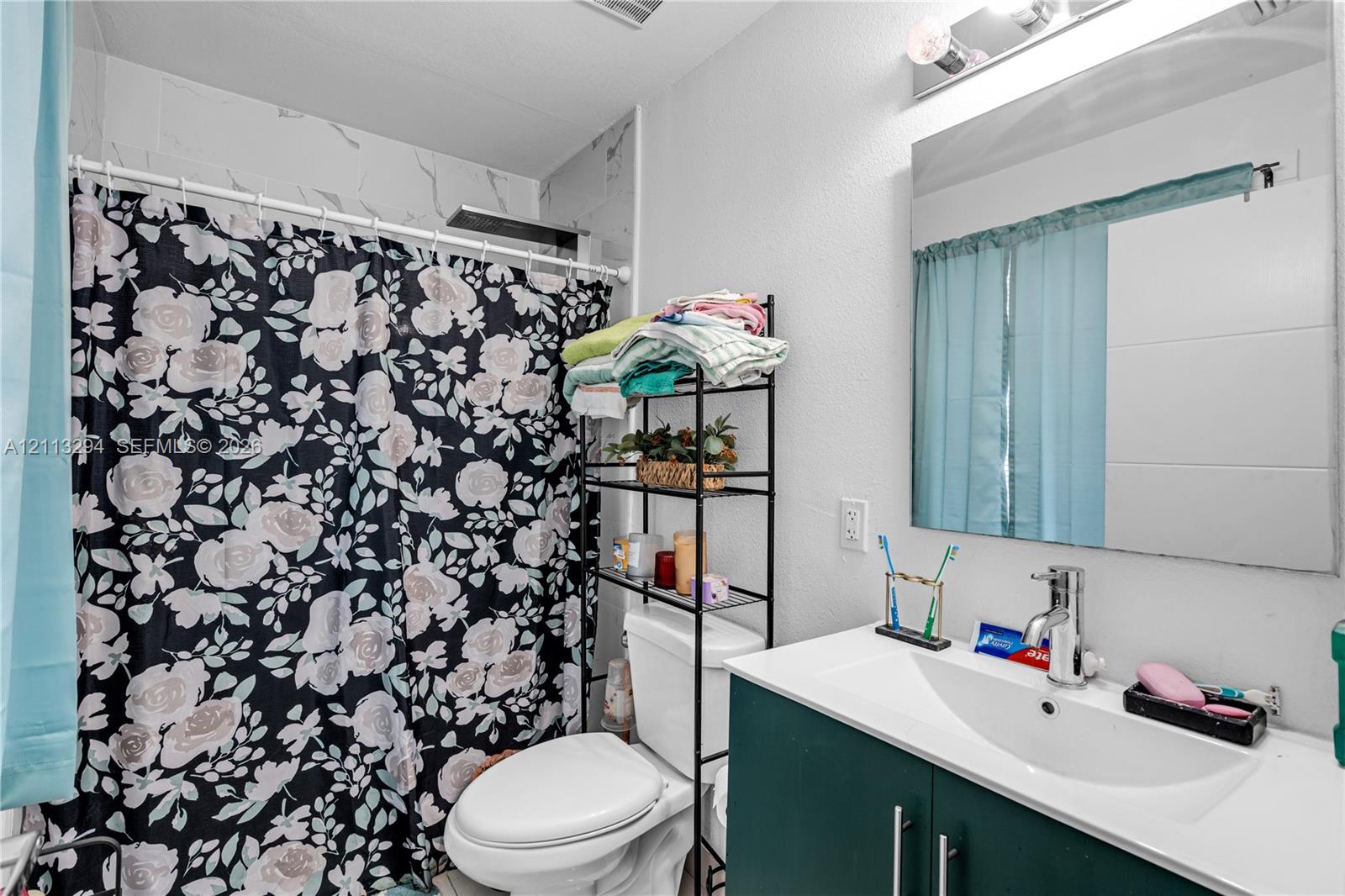 Bathroom featuring a vanity with an integrated basin, chrome faucet, wall-mounted mirror, and a shower area with tiled wall surround
