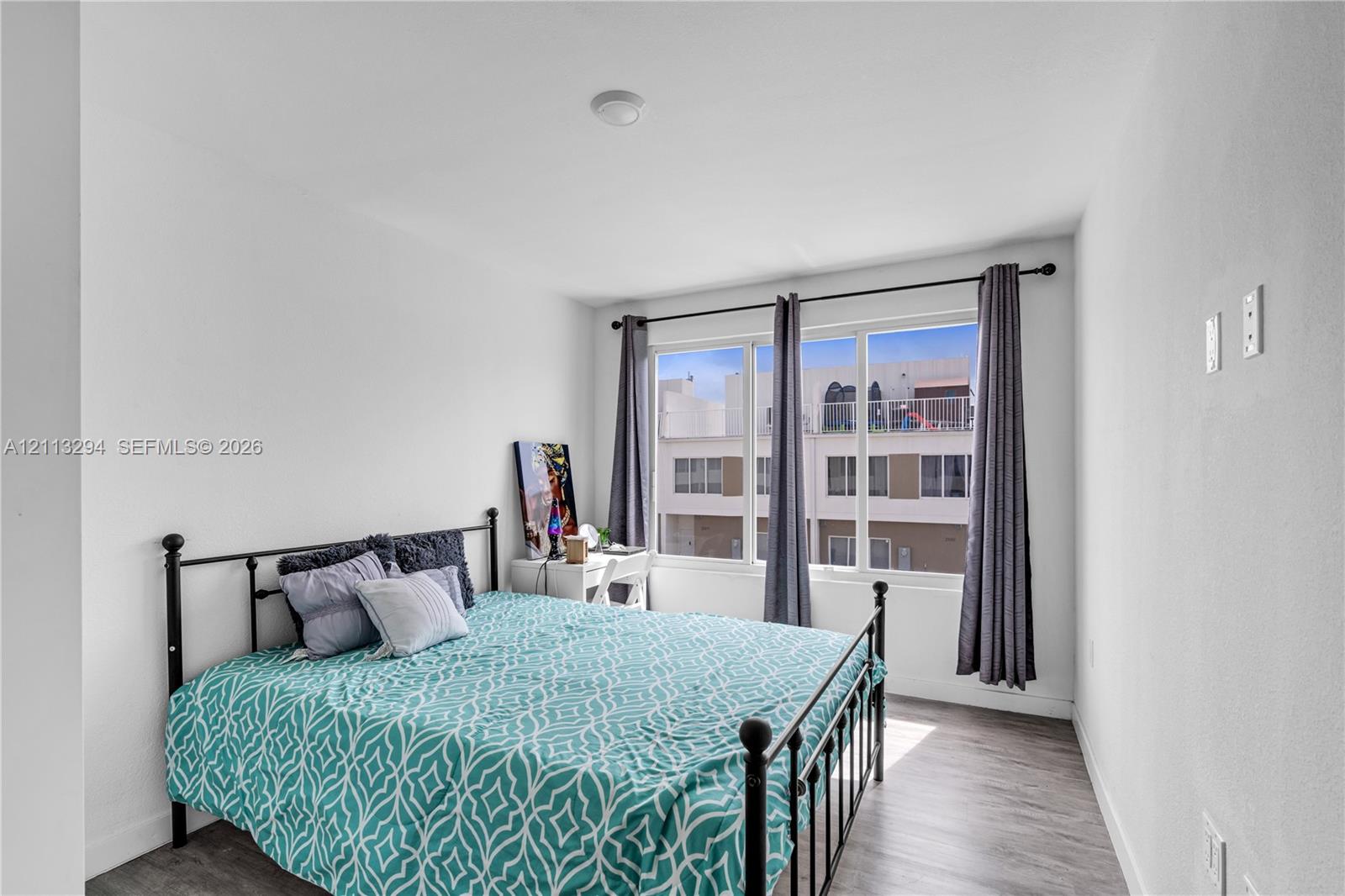 Neutral-toned room featuring wood-finish flooring, white walls, and a multi-pane window with a black curtain rod