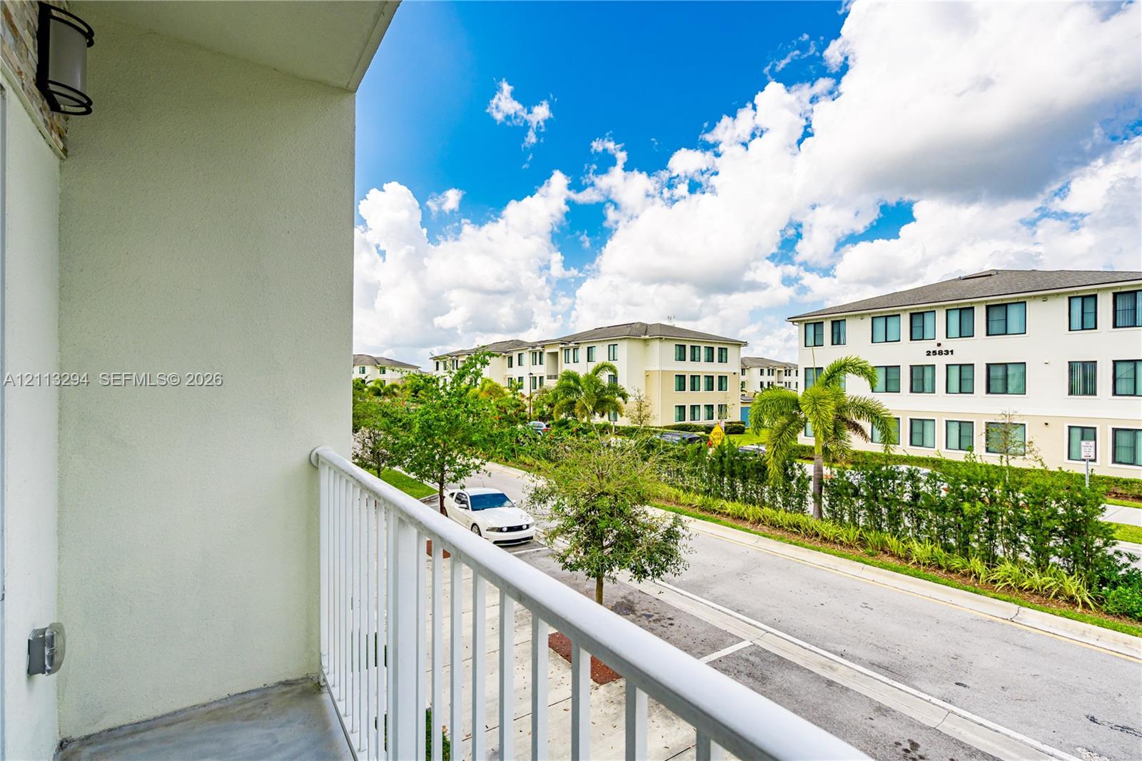Covered balcony featuring concrete flooring, white metal railing, and wall-mounted exterior lighting