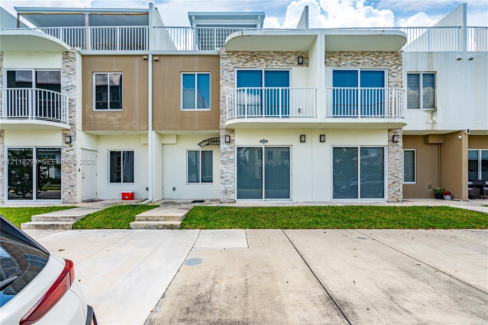 Multi-level exterior facade featuring stone veneer detailing, metal balcony railings, sliding glass door entryways, and concrete paved parking Multi-level exterior facade featuring stone veneer detailing, metal balcony railings, sliding glass door entryways, and concrete paved parking