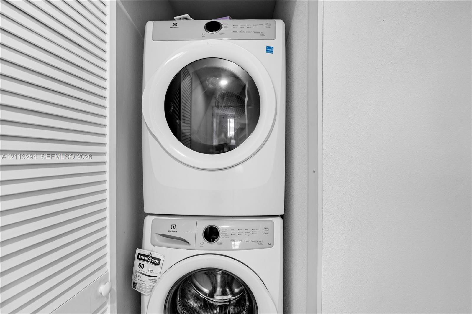 Stackable white front-load washer and dryer unit enclosed within a louvered-door closet
