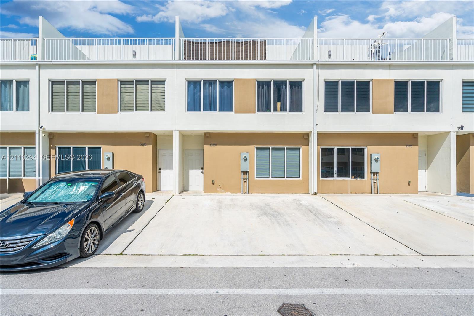 Multi-level townhome exterior featuring a smooth stucco facade, concrete driveway, and a top-level rooftop terrace with metal railings Multi-level townhome exterior featuring a smooth stucco facade, concrete driveway, and a top-level rooftop terrace with metal railings