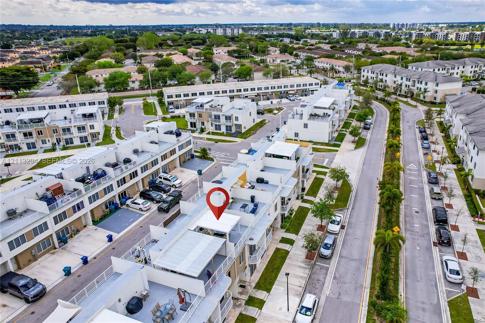Aerial perspective of multi-level townhome featuring a rooftop terrace, metal railings, and paved surface parking Aerial perspective of multi-level townhome featuring a rooftop terrace, metal railings, and paved surface parking