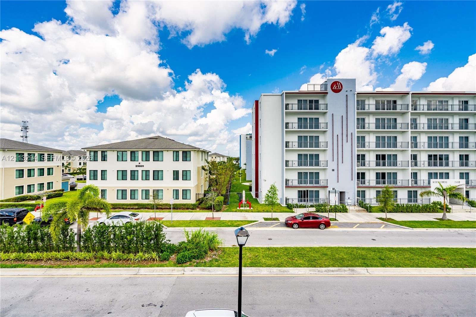 Multi-story residential complex featuring concrete facade, private balconies, paved surface parking, and manicured perimeter landscaping