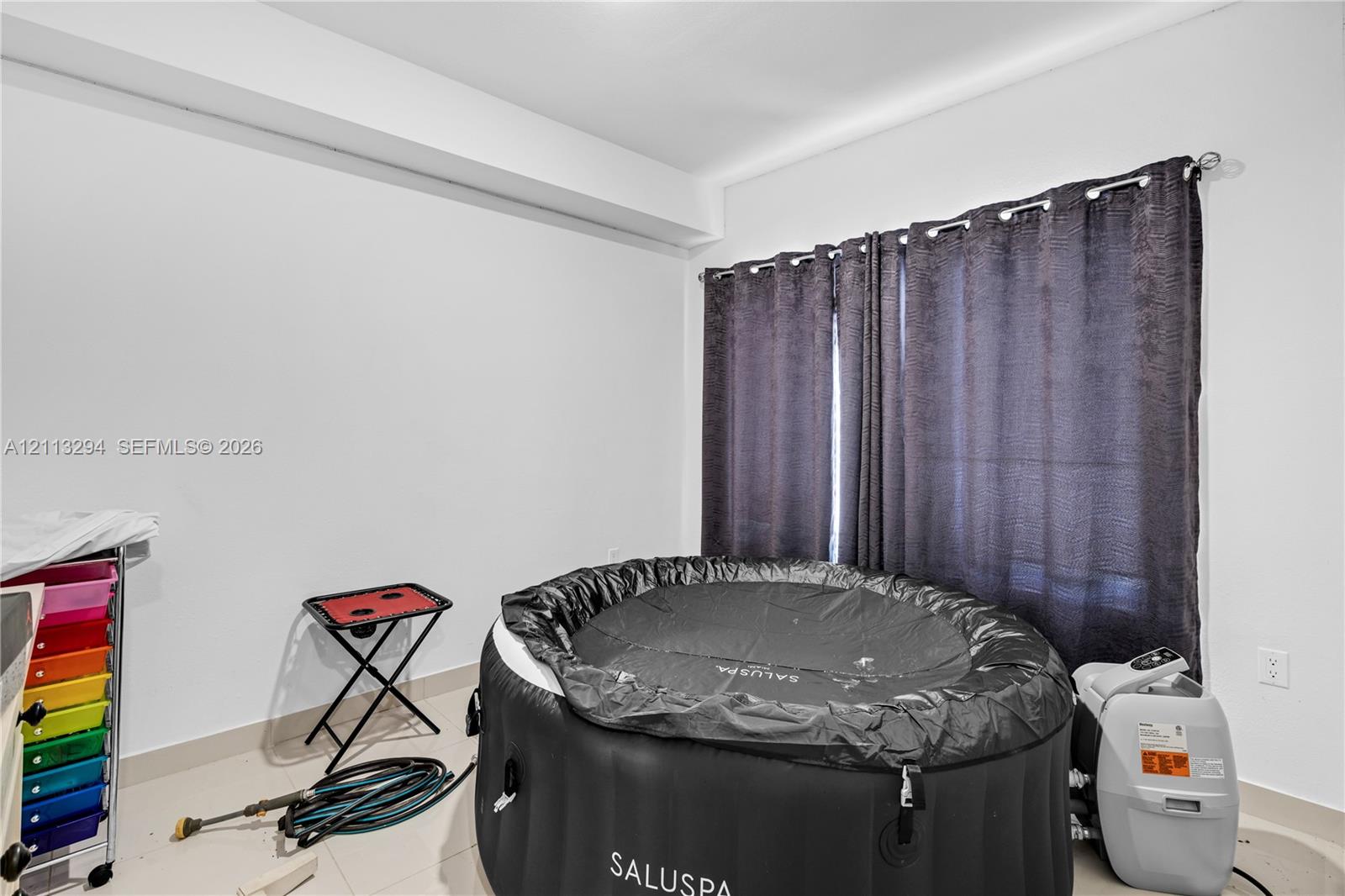 Interior space featuring tile flooring, neutral walls, and a window with hardware-mounted curtain rods