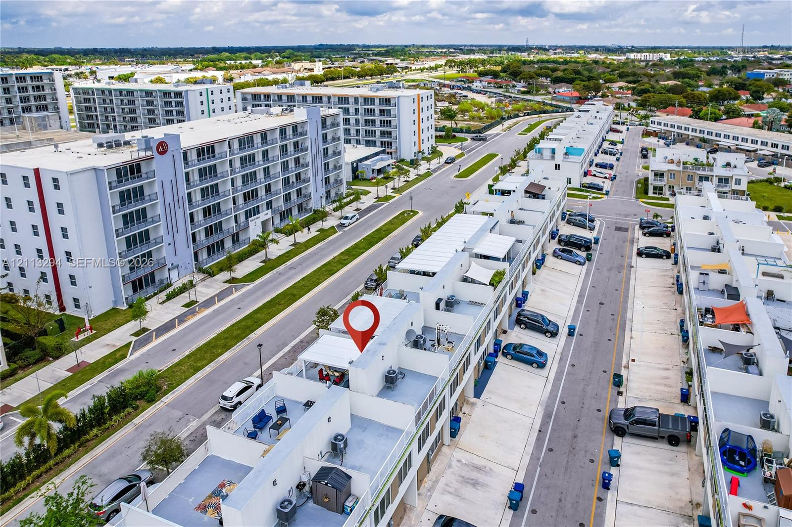 Aerial perspective of a multi-level townhome featuring a rooftop terrace, concrete construction, paved parking surface, and individual exterior utility units Aerial perspective of a multi-level townhome featuring a rooftop terrace, concrete construction, paved parking surface, and individual exterior utility units
