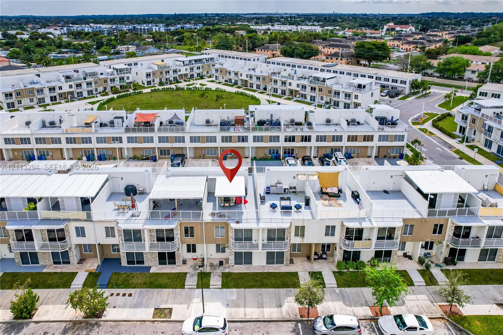 Aerial perspective of a multi-level residential complex featuring tiered roof terraces, white metal railings, stone veneer accents, and paved parking areas