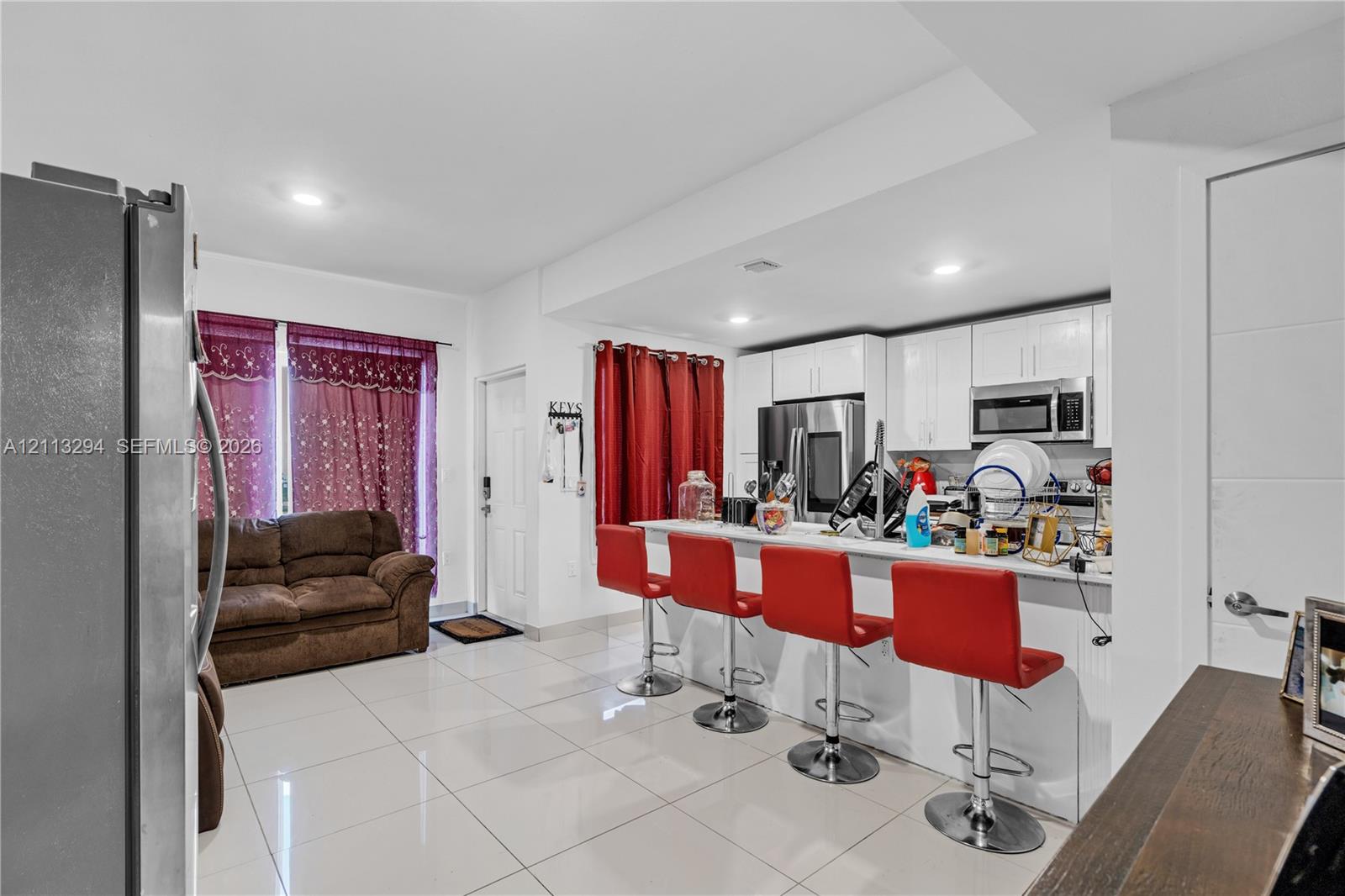 Open-concept kitchen featuring high-gloss white cabinetry, polished tile flooring, stainless steel appliances, and a breakfast bar