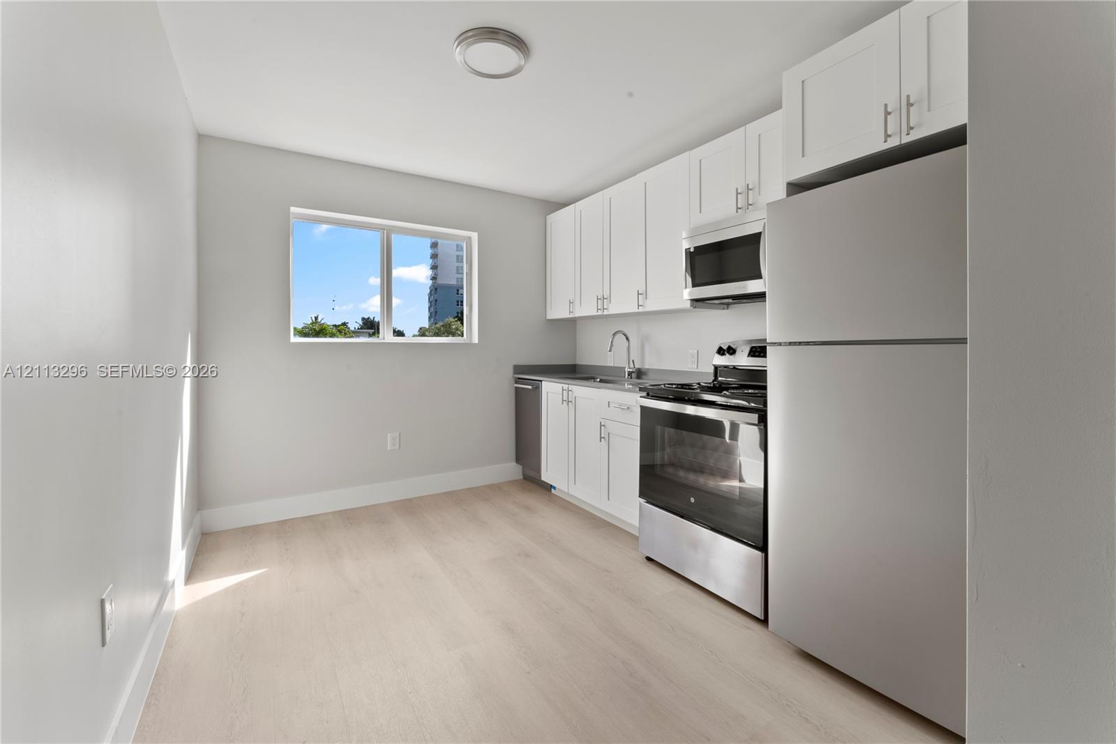 Kitchen featuring white shaker-style cabinetry, stainless steel appliances, a single-basin sink, and wood-finish flooring Kitchen featuring white shaker-style cabinetry, stainless steel appliances, a single-basin sink, and wood-finish flooring