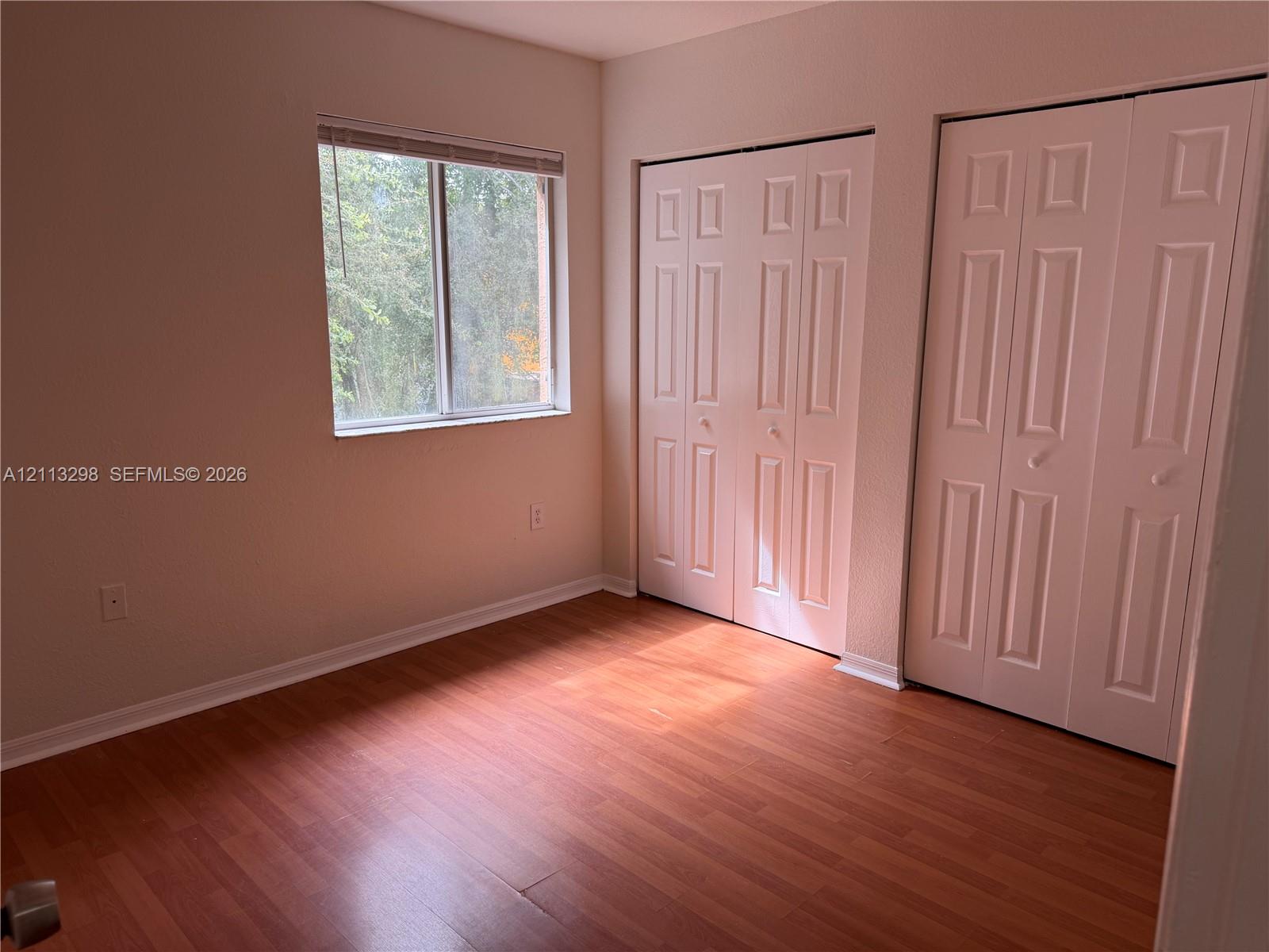 Room featuring wood-finish flooring, dual bifold closet doors, and a single-pane sliding window