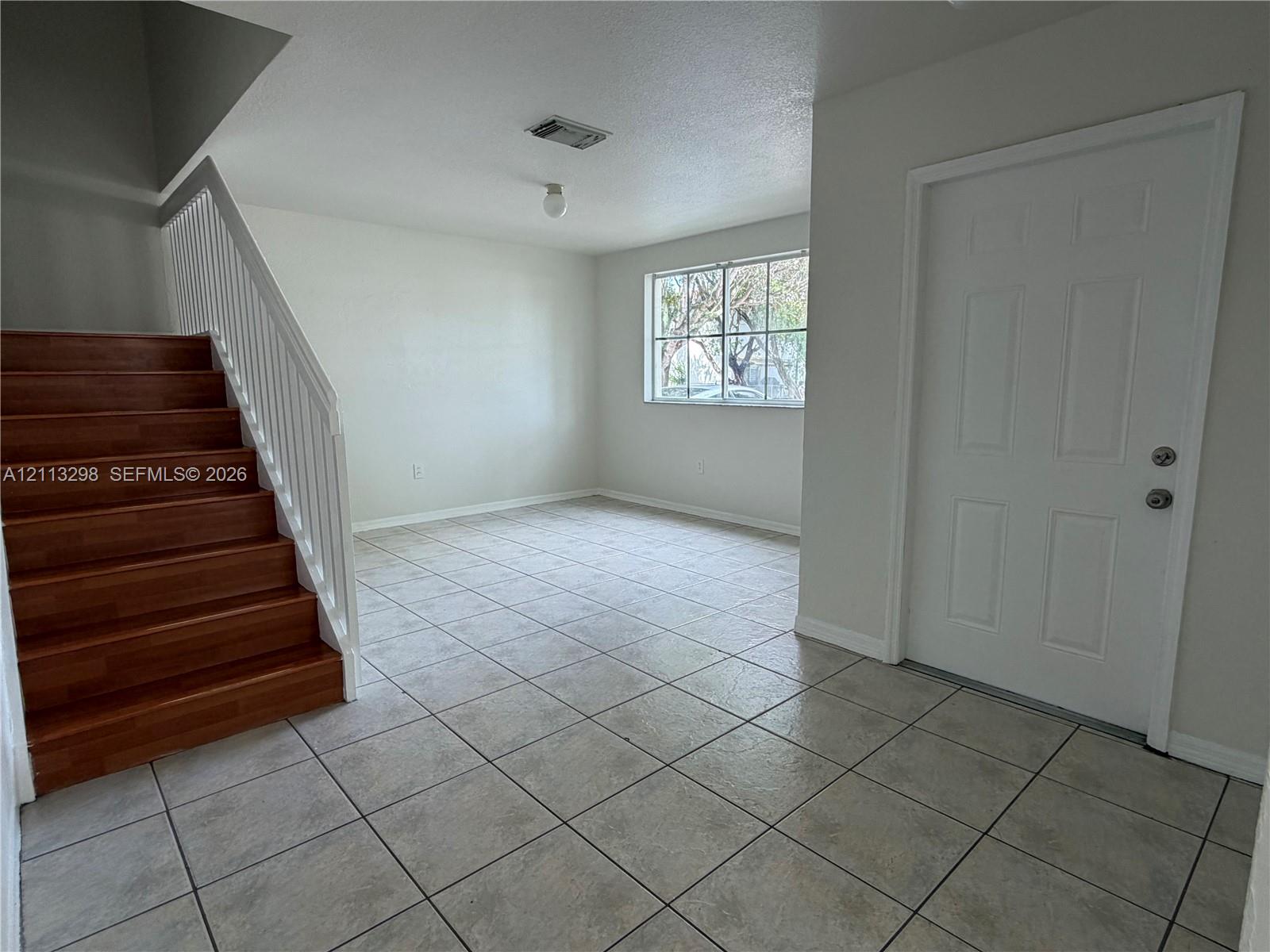 Neutral-toned tile flooring, staircase with wood-finish treads, white metal handrail, and multi-panel entry door