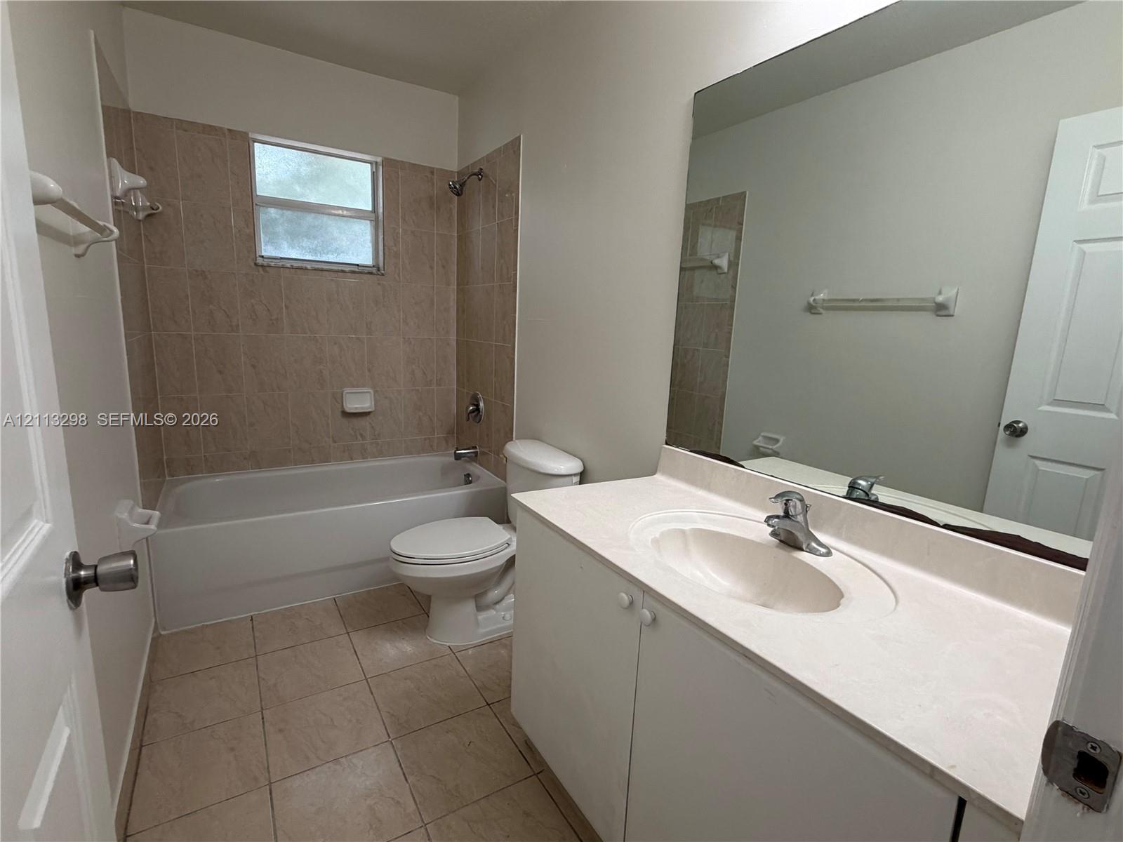 Bathroom featuring a vanity with a solid-surface countertop, an integrated sink, full-width mirror, tile flooring, and a tiled shower-tub enclosure
