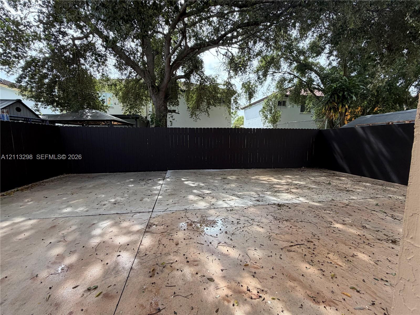 Concrete patio area enclosed by a dark wood-finish privacy fence with mature tree canopy overhead