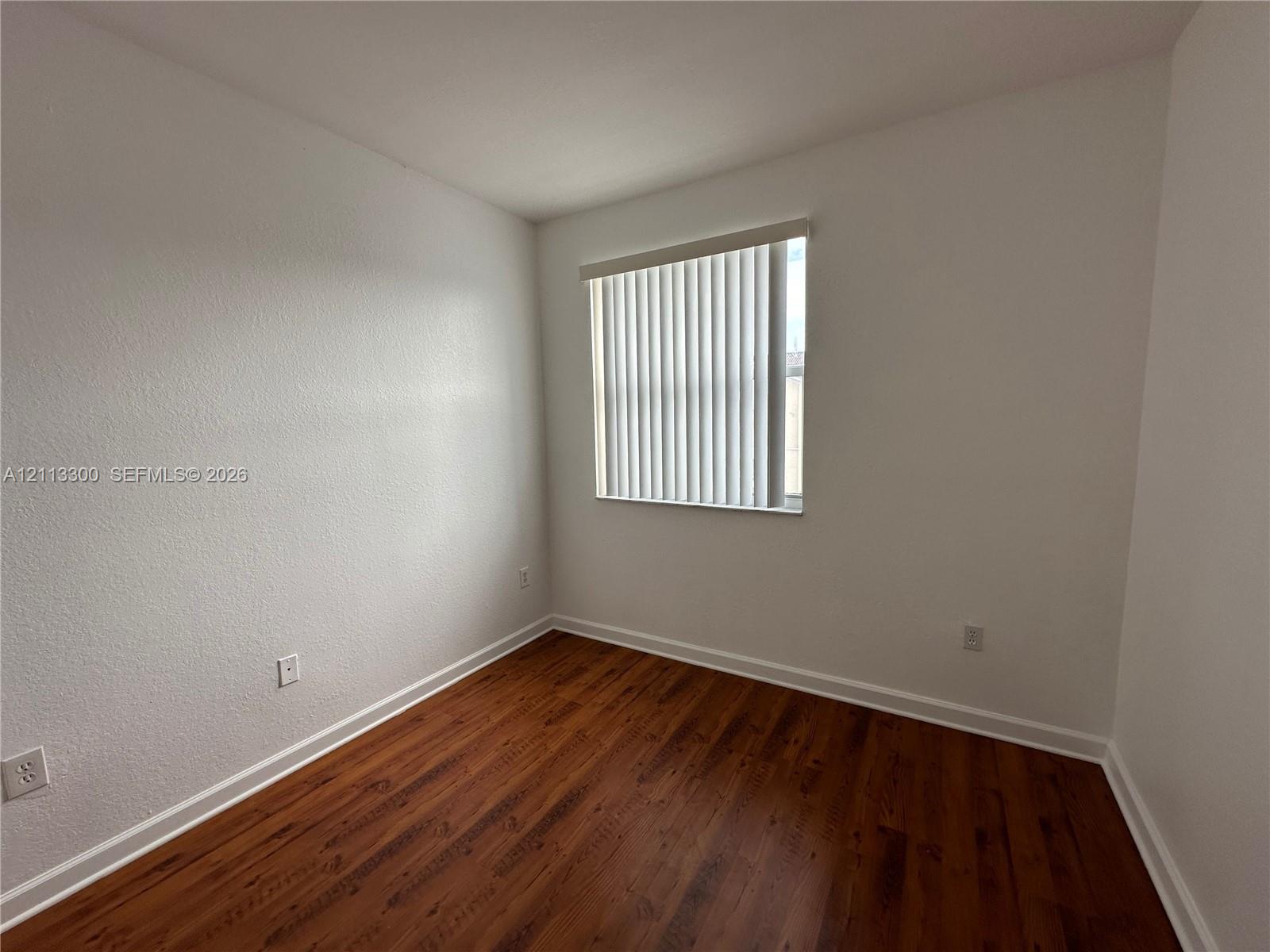 Interior room featuring wood-finish flooring, white walls, and a window with vertical blinds