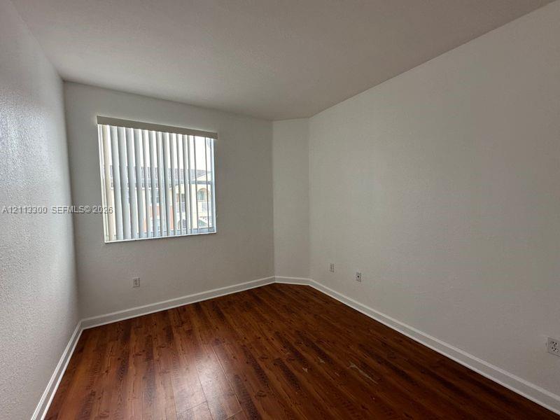 Room featuring wood-finish flooring, white walls, and a window with vertical blinds