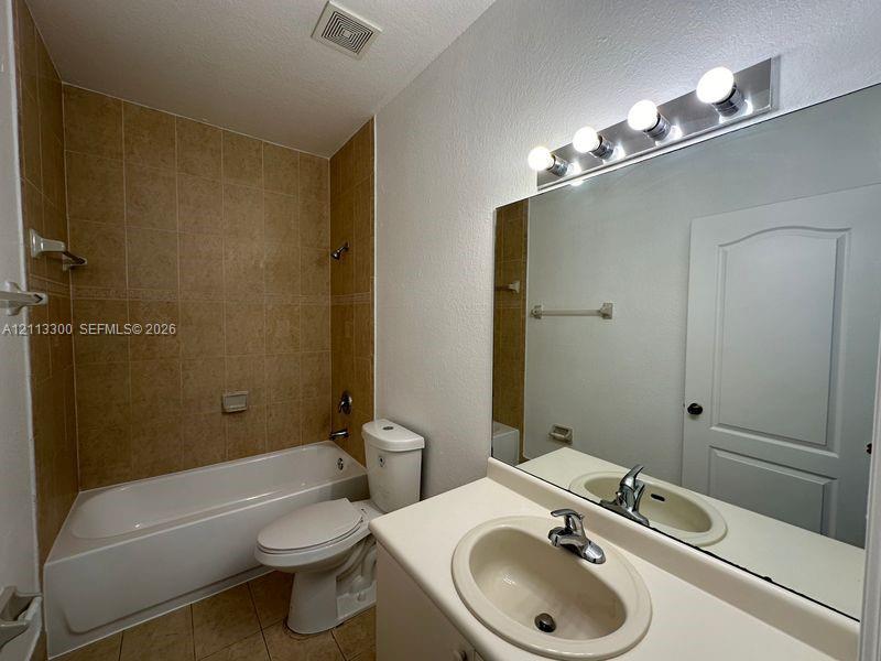 Bathroom featuring a tile-surround bathtub, vanity with a molded integrated sink, large wall-mounted mirror, and four-light fixture