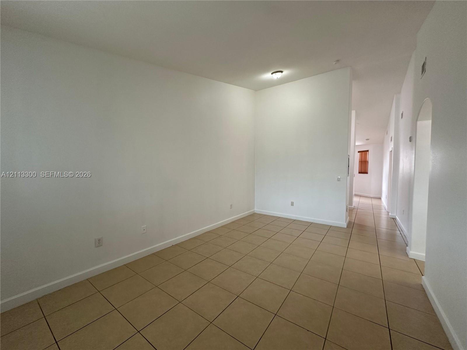 Neutral interior space featuring high ceilings, neutral wall tones, ceramic tile flooring, and an arched doorway