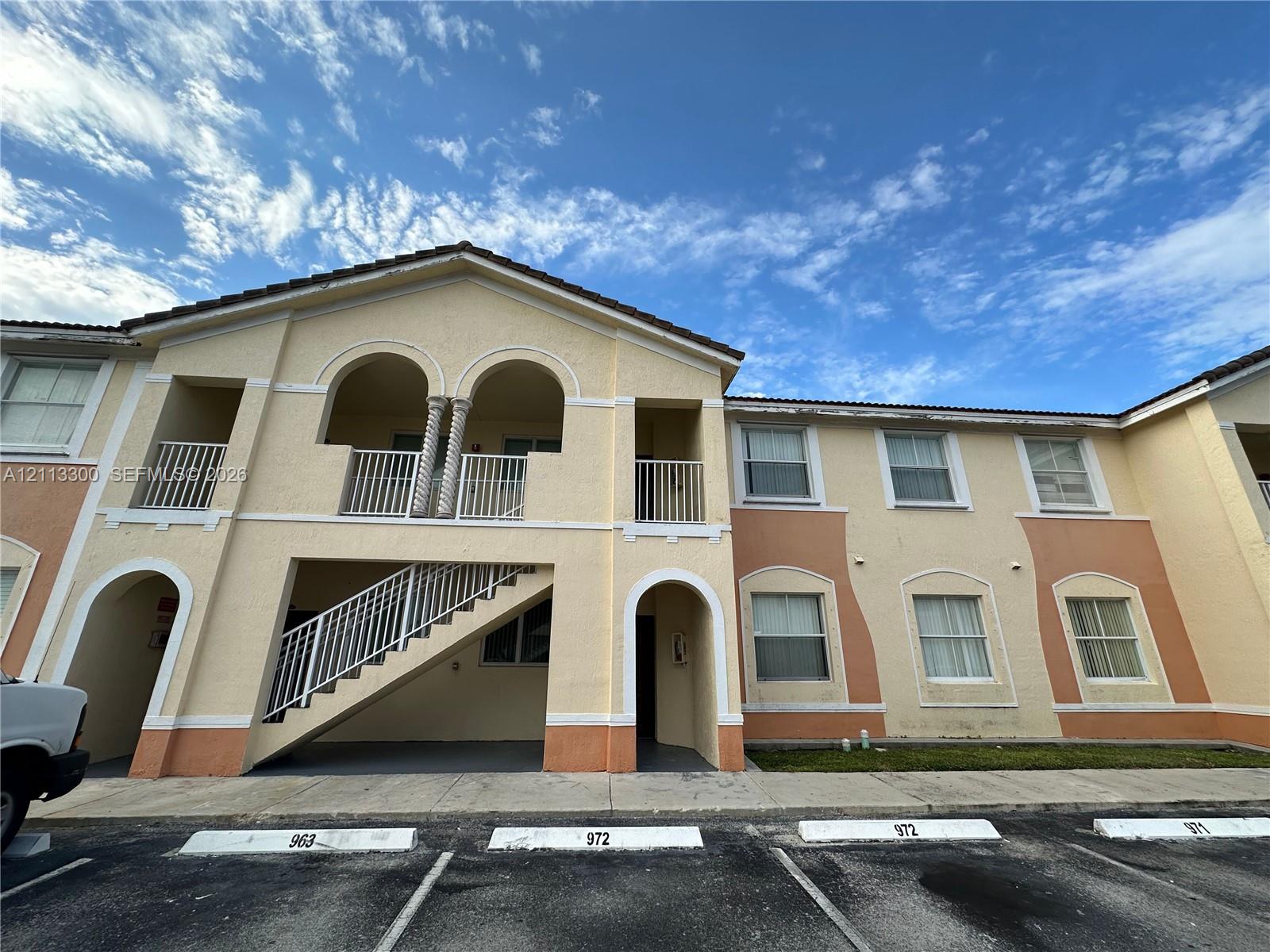 Two-story exterior featuring stucco siding, arched entryways, second-story balcony with columns, and a concrete staircase with metal railing Two-story exterior featuring stucco siding, arched entryways, second-story balcony with columns, and a concrete staircase with metal railing