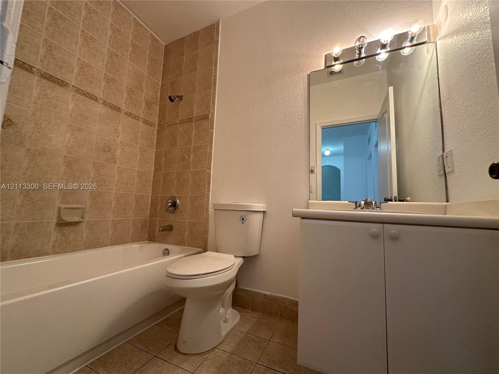 Bathroom featuring a tiled tub-shower surround, white vanity cabinet with a neutral countertop, built-in mirror with integrated lighting, and tile flooring