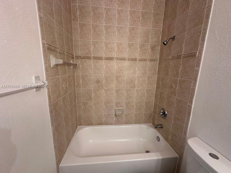 Bathtub with surround featuring neutral-toned tile, decorative accent trim, integrated soap niche, and chrome-finish hardware