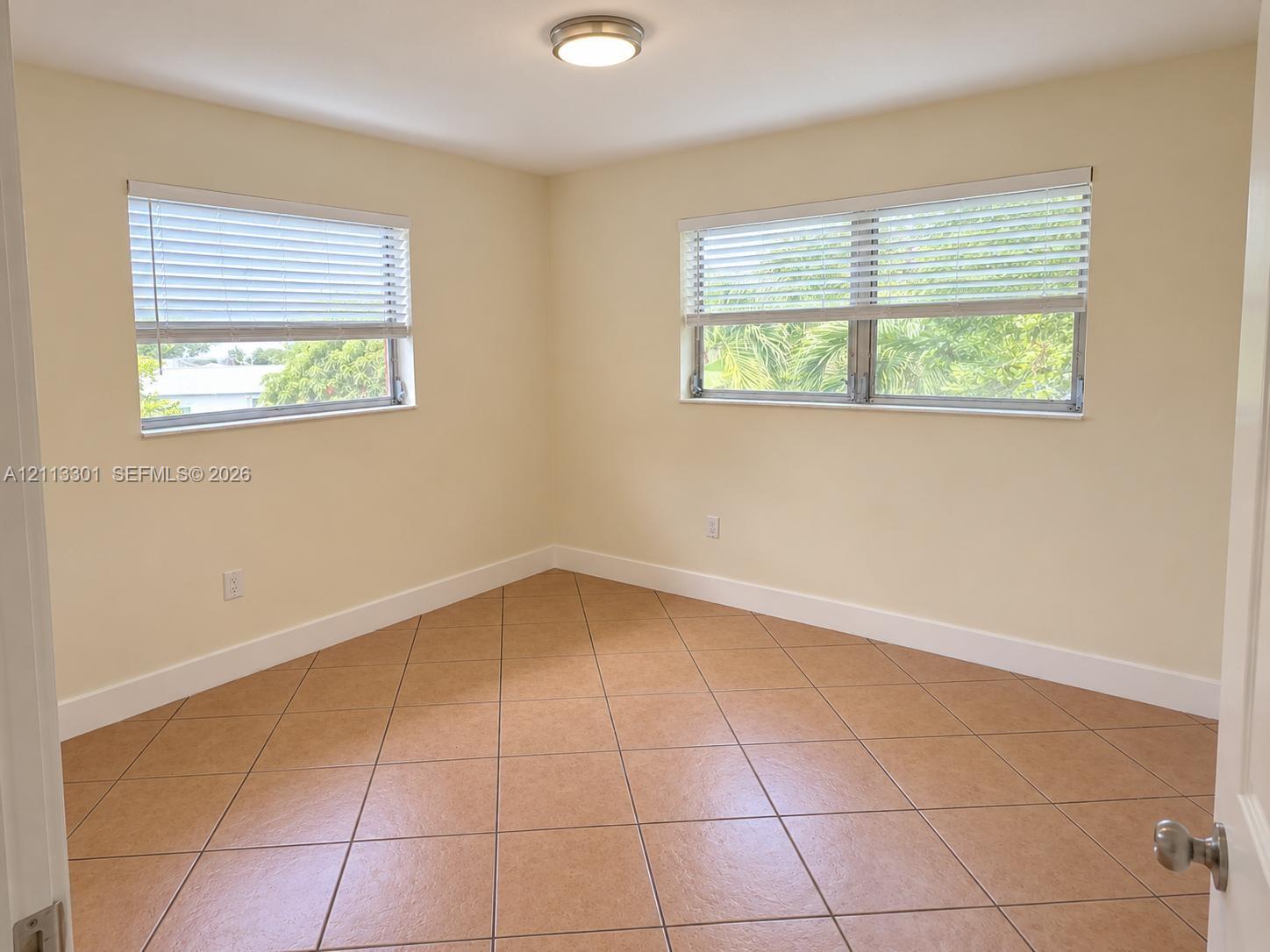 Neutral-toned interior featuring ceramic tile flooring, two horizontal windows with fitted blinds, and a flush-mount ceiling light fixture