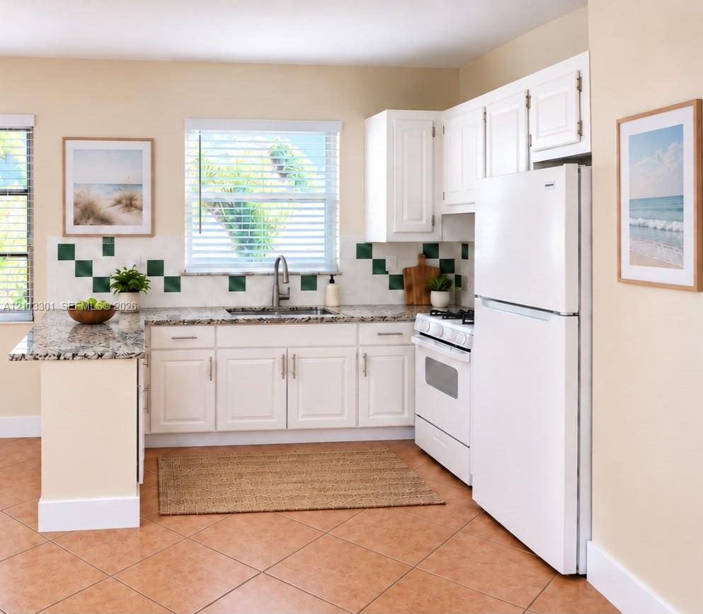Kitchen featuring white shaker-style cabinetry, stone-finish countertops, decorative tile backsplash, stainless steel sink with pull-down faucet, and neutral tile flooring Kitchen featuring white shaker-style cabinetry, stone-finish countertops, decorative tile backsplash, stainless steel sink with pull-down faucet, and neutral tile flooring