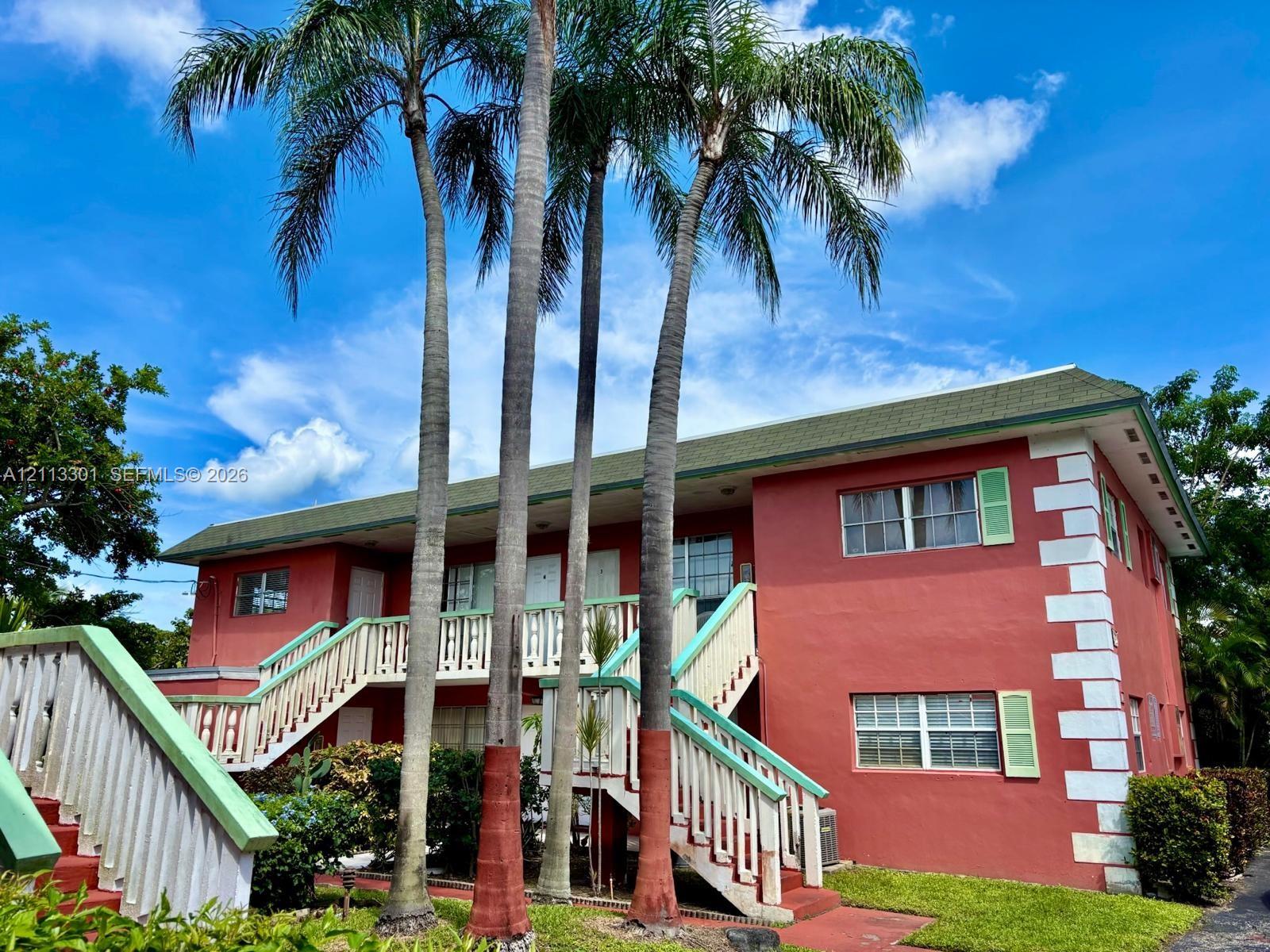 Two-story exterior featuring a stucco facade, quoined corners, a low-pitch roof, external staircases with railings, and established palm trees