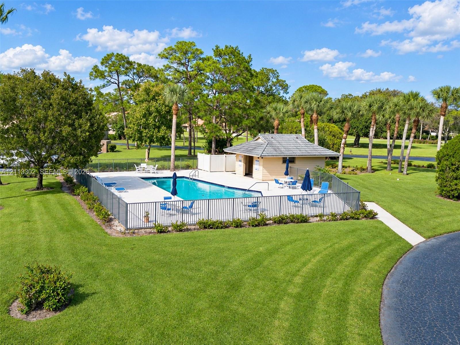 In-ground swimming pool featuring a concrete deck, metal perimeter fencing, and a detached pool house with a shingle roof