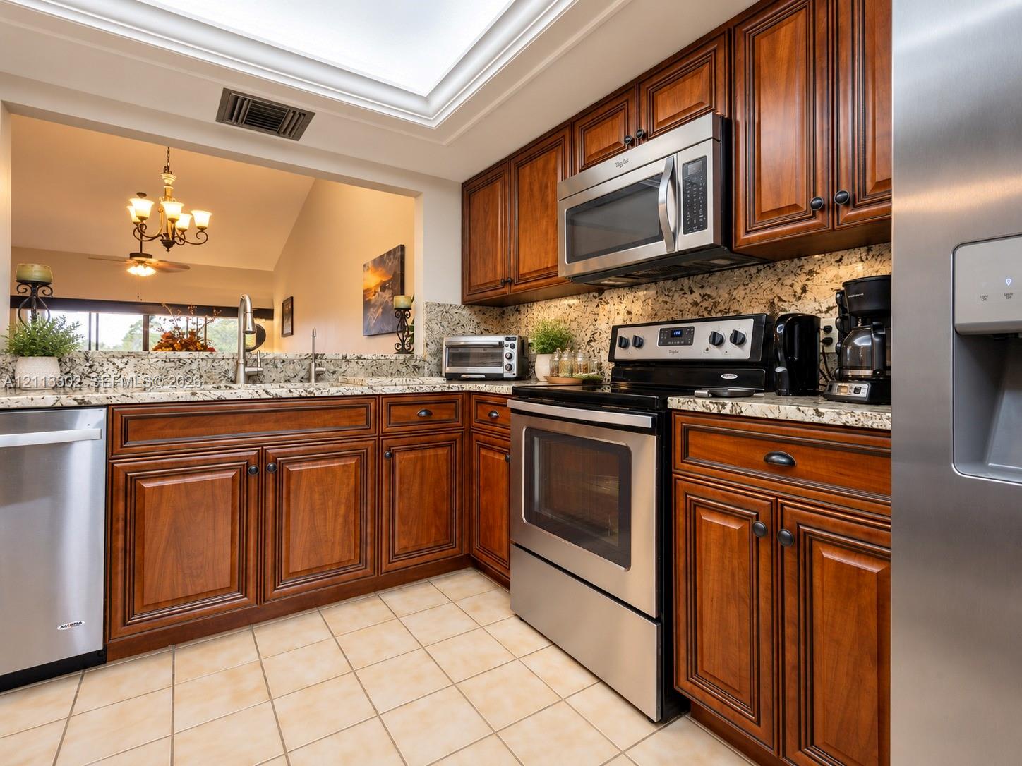 Kitchen featuring stained wood cabinetry, stone countertops, stainless steel appliances, and a recessed ceiling skylight