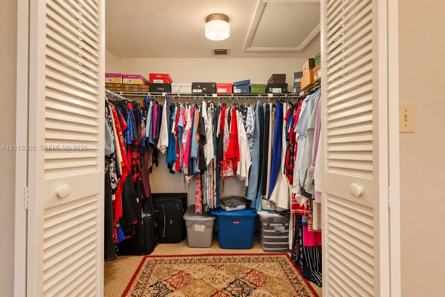 Storage closet featuring white louvered doors, wire shelving, and a central flush-mount ceiling light fixture