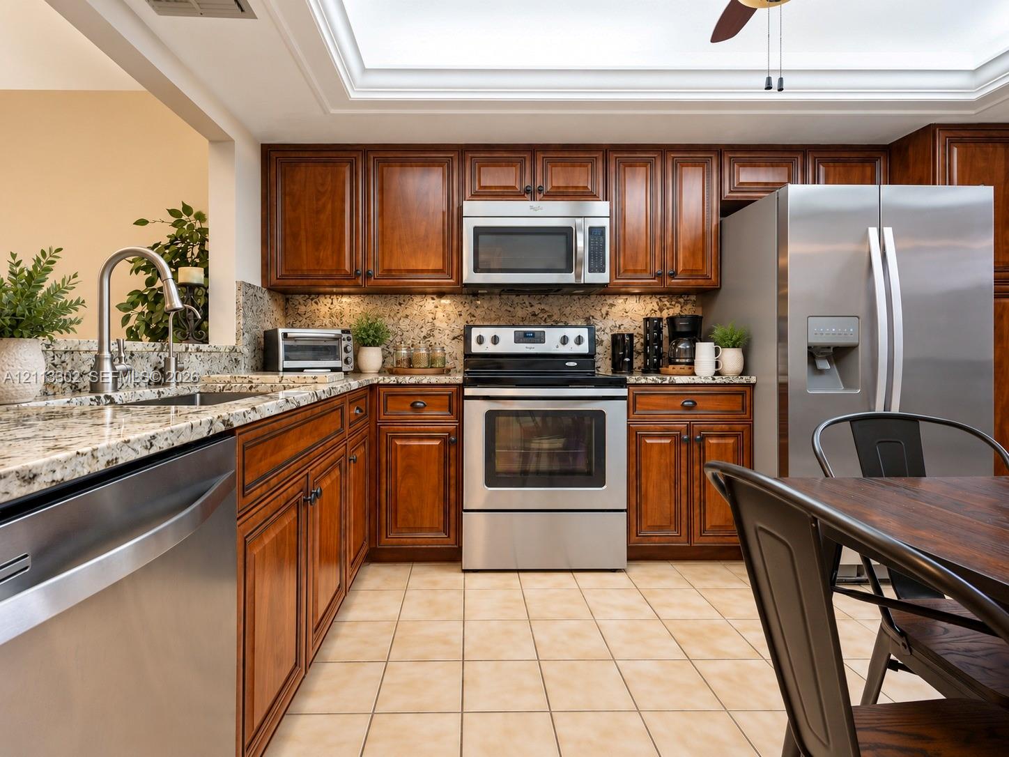 Kitchen featuring stained wood cabinetry, stone countertops, stainless steel appliances, a skylight, and tile flooring
