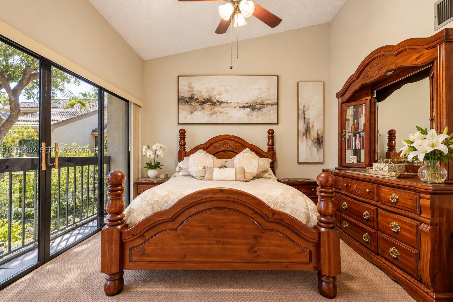 Vaulted ceilings, ceiling fan with integrated lighting, and large sliding glass doors opening to a balcony with metal railings