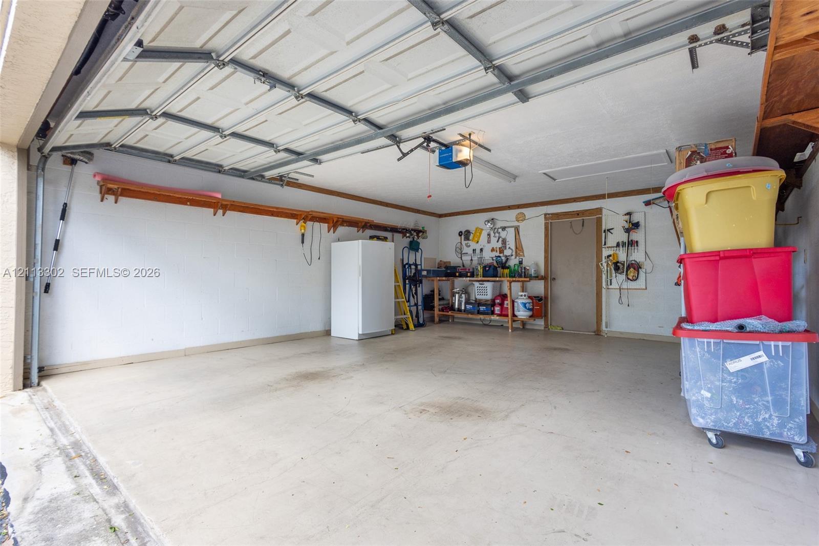 Multi-car garage featuring a concrete floor, overhead automatic door, and wall-mounted storage shelving