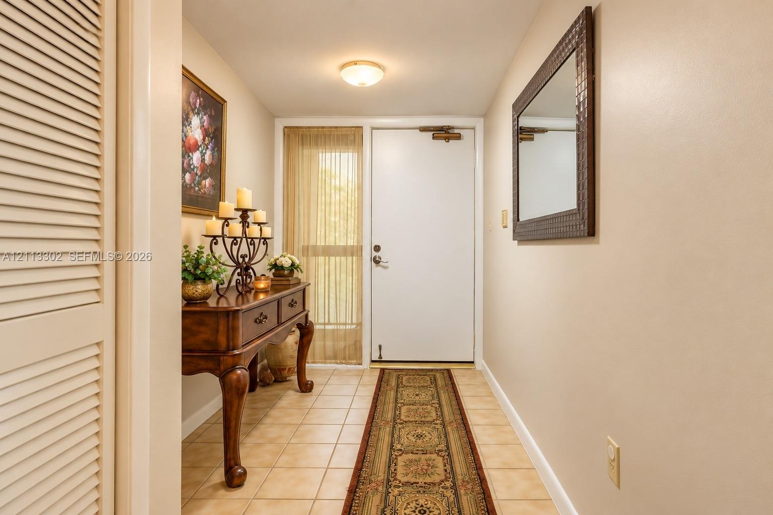Entryway featuring neutral-toned tile flooring, louvered closet doors, and a glass-paneled sidelight with vertical blinds