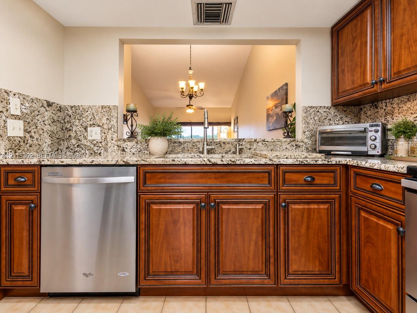 Kitchen featuring natural stone countertops, tile backsplash, warm-toned wooden cabinetry, and stainless steel dishwasher