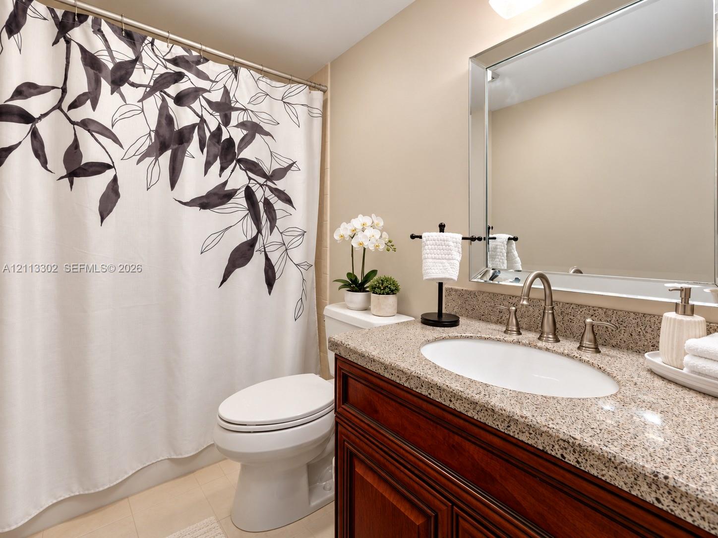 Bathroom vanity featuring a stone-composite countertop, undermount sink, gooseneck faucet, wooden cabinetry, and a large rectangular mirror with a beveled frame