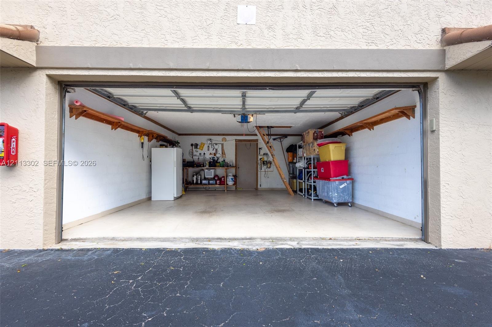 Attached two-car garage featuring painted masonry walls, overhead sectional door, built-in wooden wall shelving, and an integrated workbench