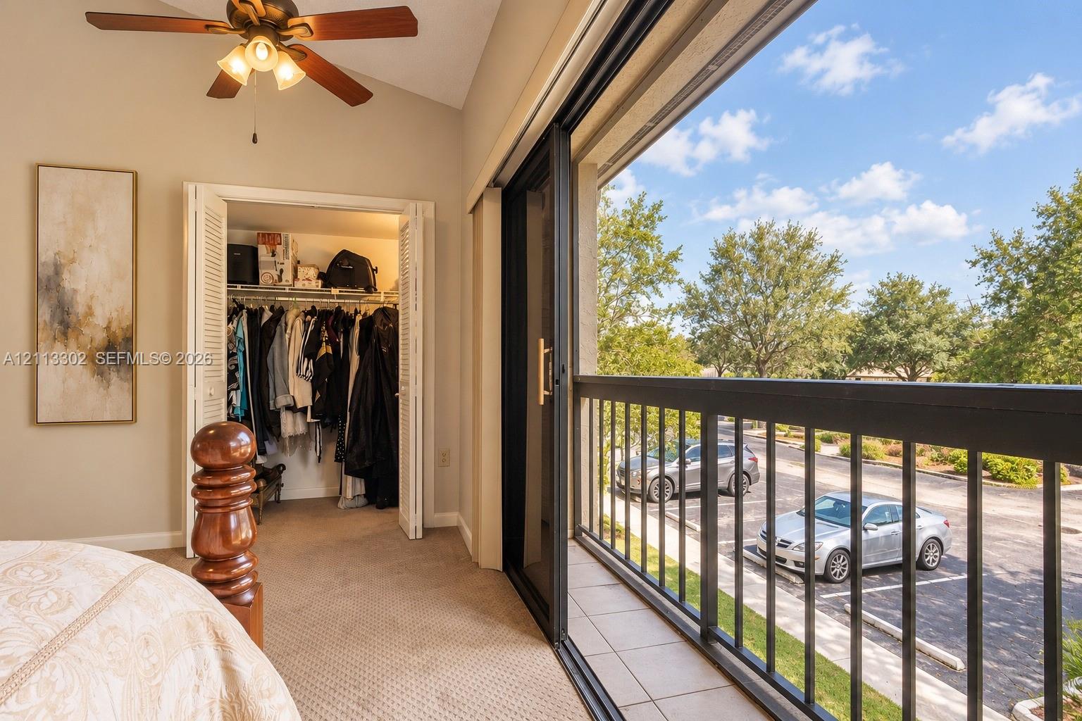 Vaulted ceiling with a central multi-blade ceiling fan, sliding glass doors, and a tiled balcony featuring black metal railings
