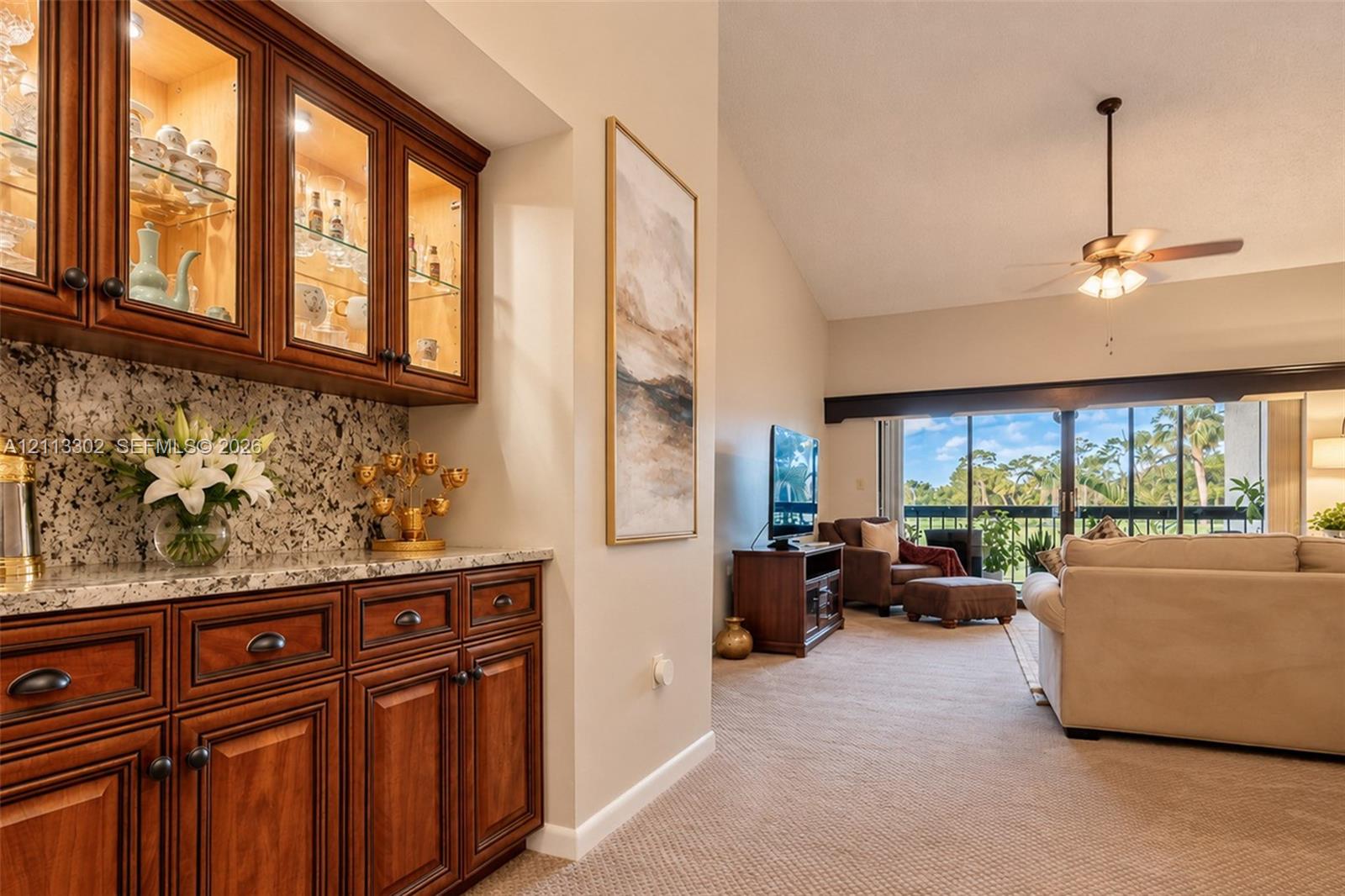 Built-in wood cabinetry with glass-front upper displays, stone countertops, vaulted ceilings, and a ceiling fan
