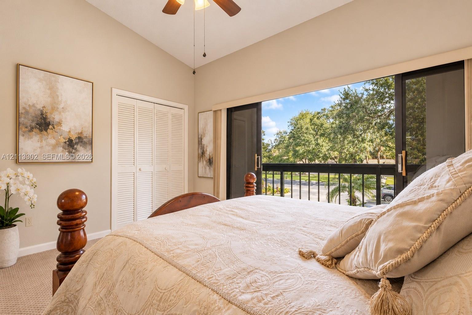 Vaulted ceiling, sliding glass doors with access to a balcony, louvered closet doors, and a ceiling fan