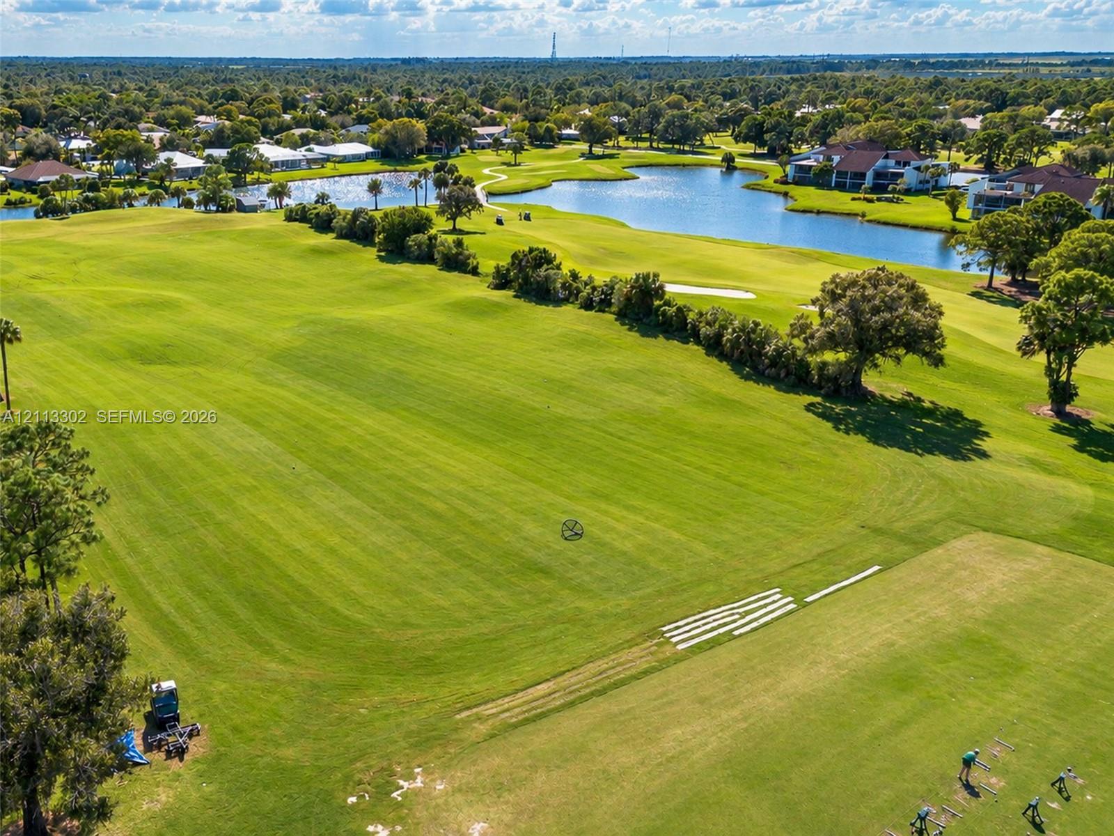 Expansive manicured lawn featuring golf course fairways, mature tree clusters, and multiple water features