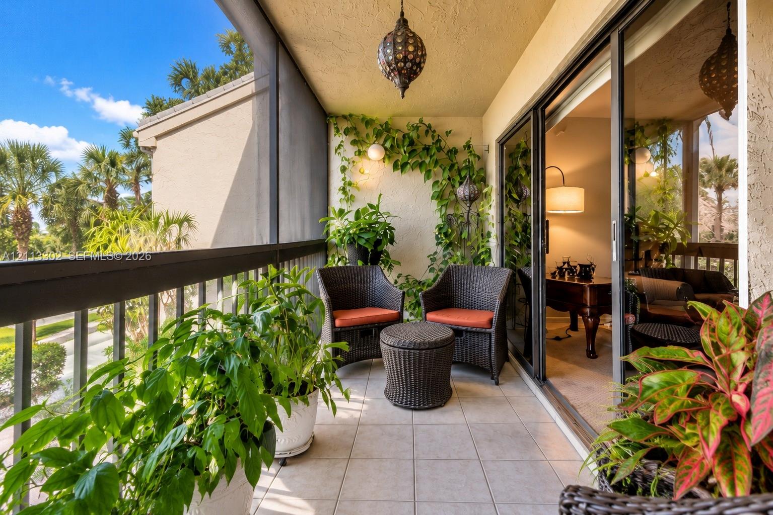 Screened balcony featuring ceramic tile flooring, a decorative metal hanging pendant light, sliding glass entry doors, and a metal railing